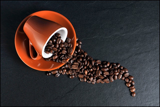 Close up of a professional coffee taster cupping session with multiple small white cups of brewed coffee on a wooden table alongside scoring sheets a silver cupping spoon and whole coffee beans scattered around