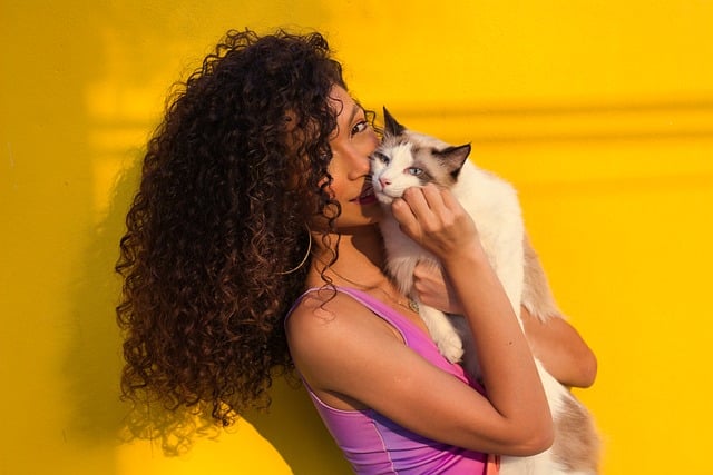 Smiling woman in her thirties with natural curly hair wearing an earth-toned blouse sitting at a computer in a bright modern office with product samples and packaging prototypes on her desk